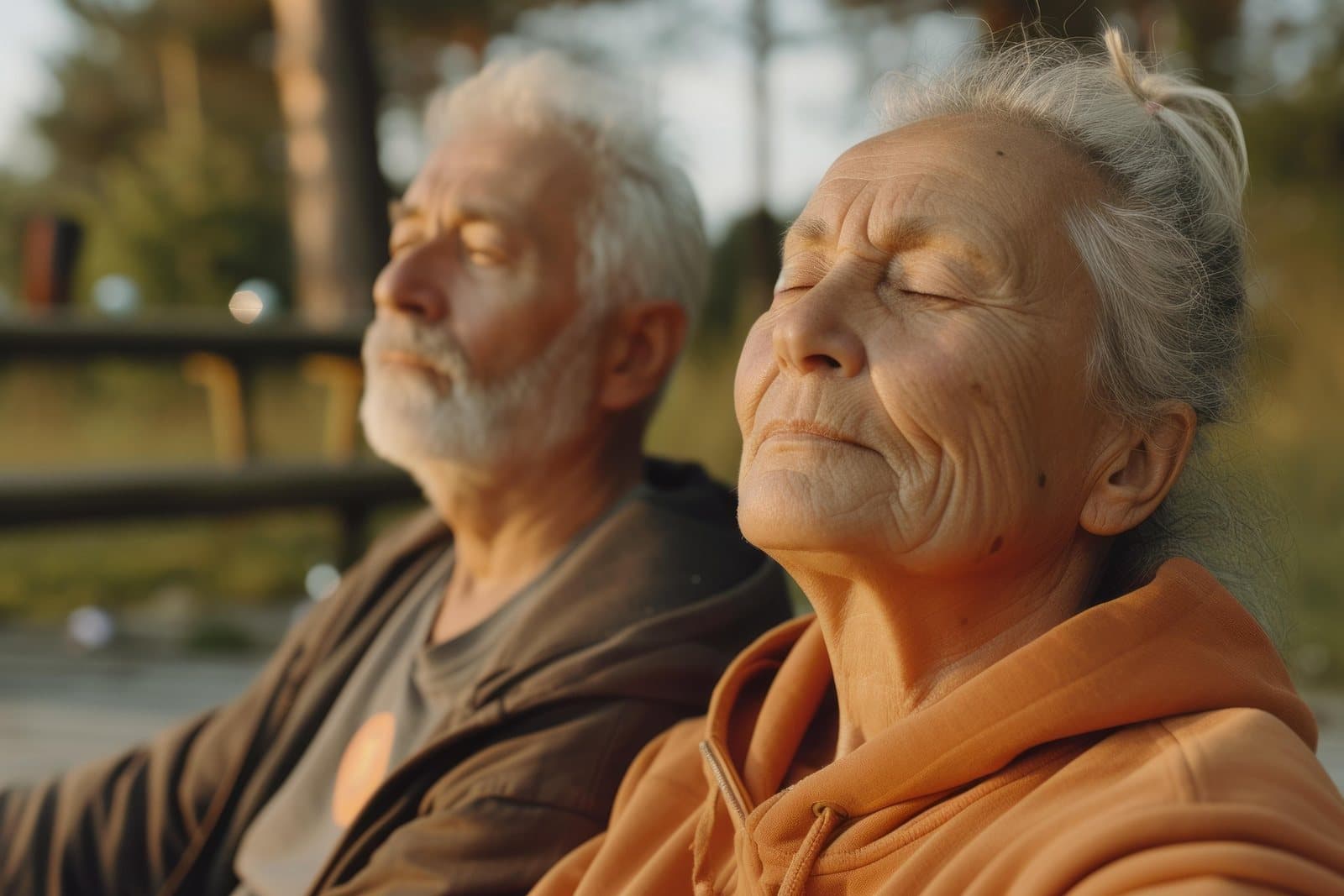 An older couple sitting outdoors in warm evening sunlight, eyes closed and content