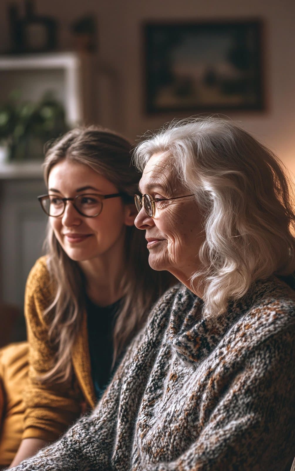An older woman and a younger woman sitting side by side at home, smiling softly