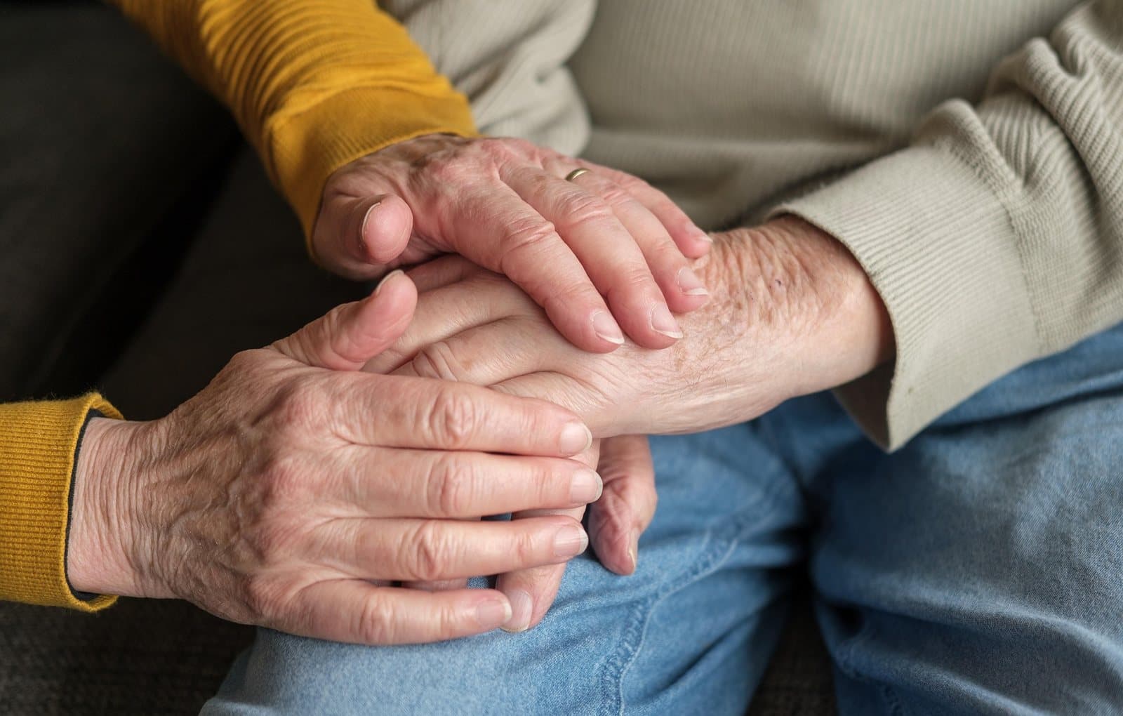 Two older people holding hands, one in a mustard sweater and one in a light knit